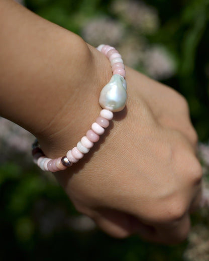 Hand wearing a pink and white pearl bracelet with a blurred natural background